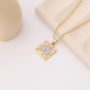 May include: Gold chain necklace with a square pendant featuring a silver-toned religious icon.