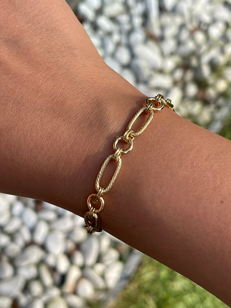 May include: A gold chain bracelet with oval links. The chain is twisted and has a polished finish.