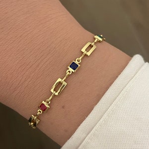 Op de afbeelding: Gouden armband met een kettinglinkontwerp en kleurrijke vierkante accenten. De armband heeft rode, blauwe en groene accenten.