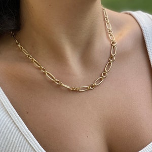 May include: A gold chain necklace with a delicate, oval-shaped link design. The necklace is worn by a person with a white tank top.