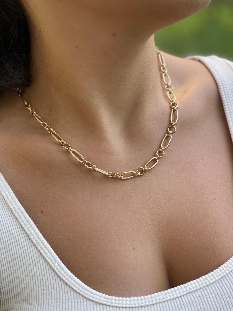 May include: A gold chain necklace with a delicate, oval-shaped link design. The necklace is worn by a person with a white tank top.