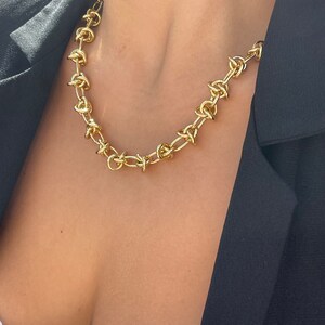 Peut inclure: Un collier en cha&icirc;ne dor&eacute;e avec un design de n&oelig;ud unique. Le collier est compos&eacute; de maillons &eacute;pais et volumineux et constitue une pi&egrave;ce forte.