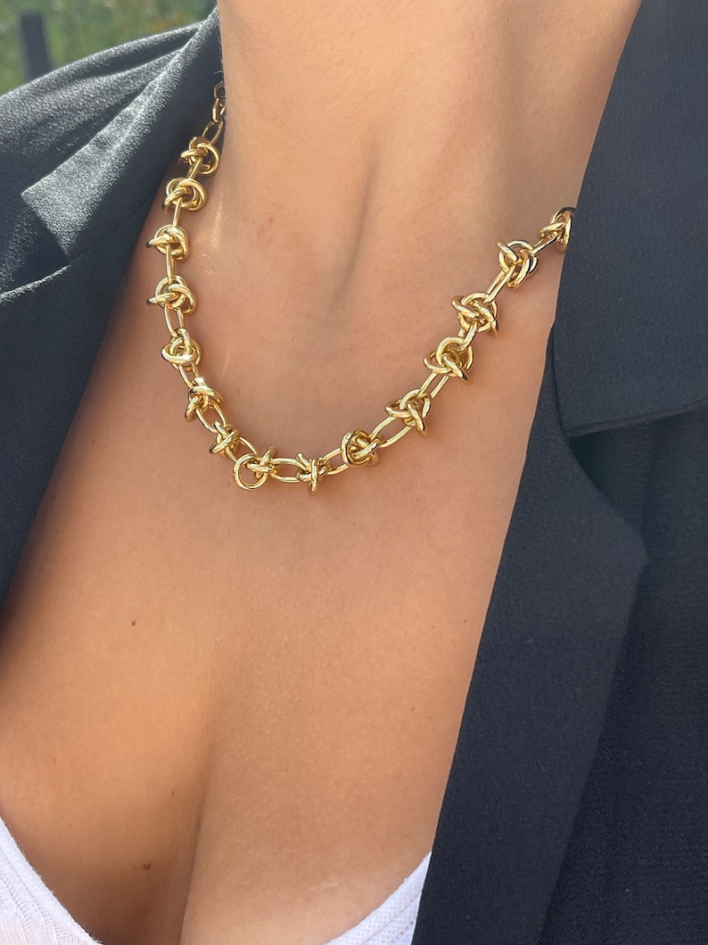 Peut inclure: Un collier en cha&icirc;ne dor&eacute;e avec un design de n&oelig;ud unique. Le collier est compos&eacute; de maillons &eacute;pais et volumineux et constitue une pi&egrave;ce forte.