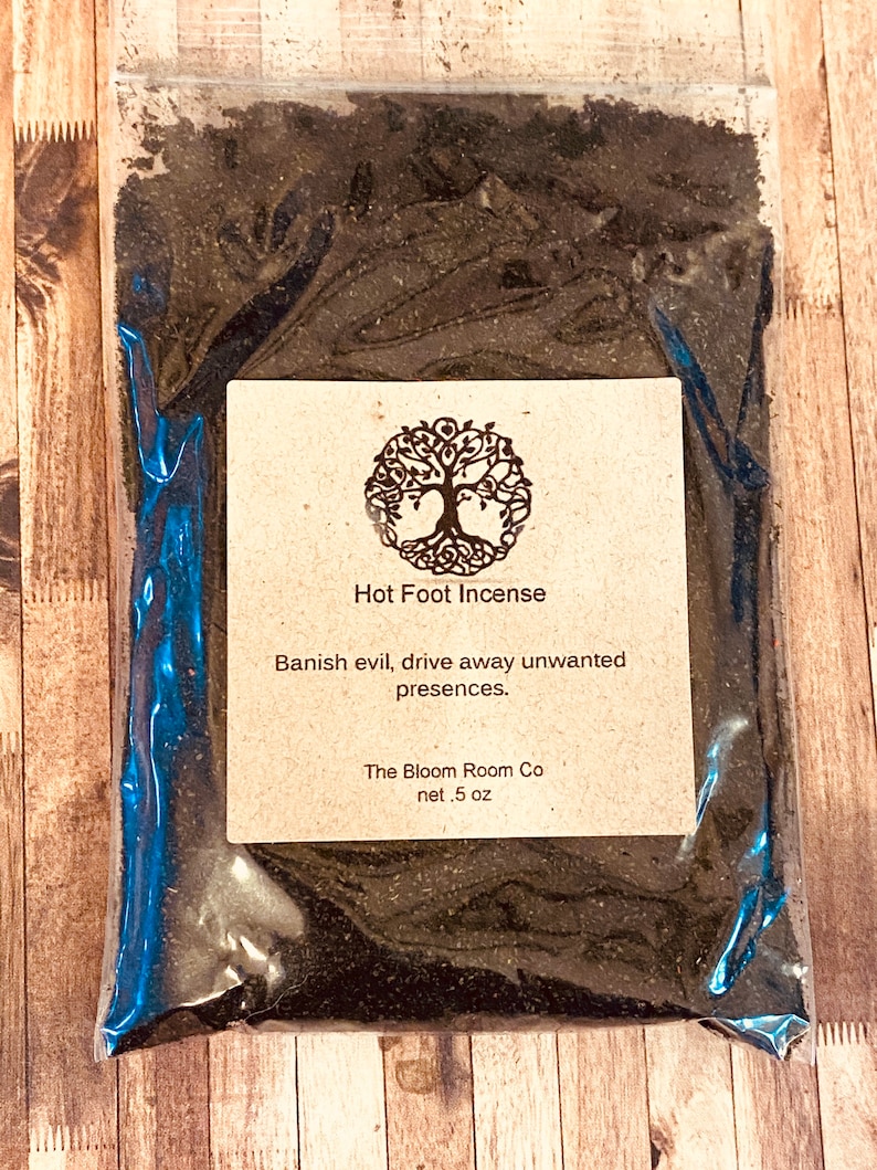Op de afbeelding: Een klein plastic zakje gevuld met zwart poeder met het label "Hot Foot Incense". Het label vermeldt ook "Banish evil, drive away unwanted presences." en "The Bloom Room Co net .5 oz".