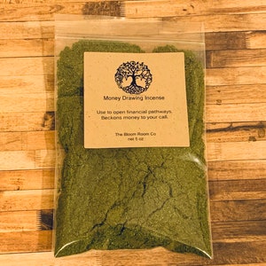 Op de afbeelding: Een kleine doorzichtige plastic zak met groene wierook met een bruin papieren etiket met de tekst "Money Drawing Incense" en de tekst "Use to open financial pathways, Beckons money to your call. The Bloom Room Co net 5 oz."