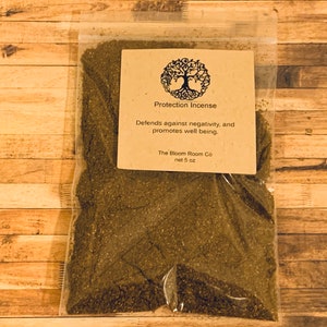 Op de afbeelding: Een bruine papieren zak gevuld met losse groene wierook. De zak heeft een label met de tekst "Protection Incense" en "Beschermt tegen negativiteit en bevordert het welzijn." Het label bevat ook de bedrijfsnaam "The Bloom Room Co" en het nettogewicht "5 oz".