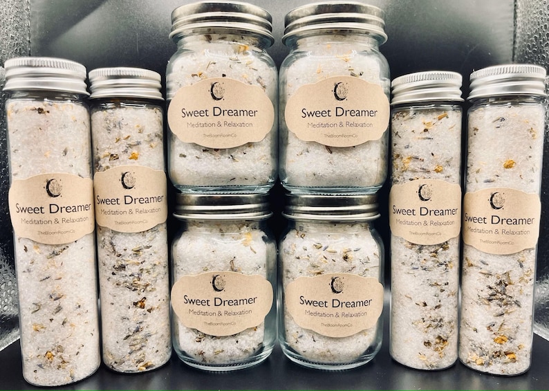 May include: An assortment of glass jars and tubes filled with bath salts. Each container has a silver lid and a label that reads "Sweet Dreamer Meditation & Relaxation." The salts are white with visible herbs and flowers.