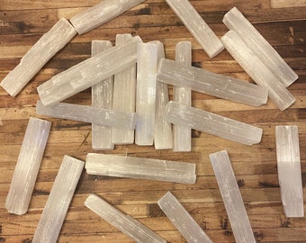 May include: A collection of white selenite wands, also known as selenite sticks, arranged on a wooden surface. The wands are smooth and polished, with a natural, crystalline texture.