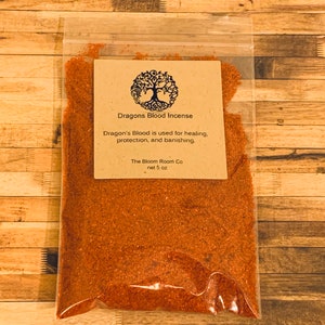 Op de afbeelding: Een kleine doorzichtige plastic zak gevuld met roodbruin Dragon's Blood wierook. De zak heeft een bruin papieren etiket met een boomlogo en de tekst "Dragons Blood Incense", "Dragon's Blood is used for healing, protection, and banishing." en "The Bloom Room Co net 5 oz".