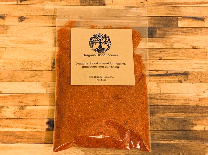 Op de afbeelding: Een kleine doorzichtige plastic zak gevuld met roodbruin Dragon's Blood wierook. De zak heeft een bruin papieren etiket met een boomlogo en de tekst "Dragons Blood Incense", "Dragon's Blood is used for healing, protection, and banishing." en "The Bloom Room Co net 5 oz".