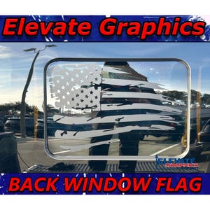 May include: A silver-colored, distressed American flag design is displayed on a vehicle's back window. The image features the text "Elevate Graphics" at the top and "Back Window Flag" at the bottom, both in red and white lettering.