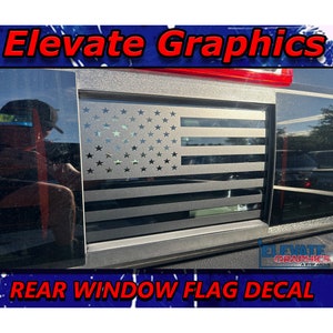 May include: A rear window flag decal featuring a grey and black American flag design. The decal is applied to a black car window. The text "Elevate Graphics" is visible at the top of the image and "REAR WINDOW FLAG DECAL" is visible at the bottom.