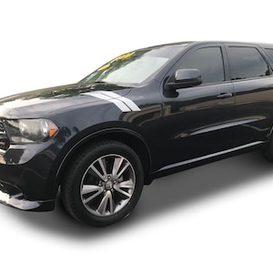 Może przedstawiać: Czarny SUV Dodge Durango z białym paskiem na masce i czarnymi kołami. Pojazd jest zaparkowany na białym tle.