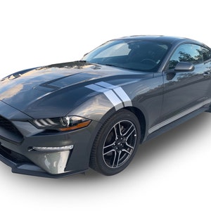 May include: A gray Ford Mustang coupe with white racing stripes on the hood and sides. The car has black wheels and a black front bumper.