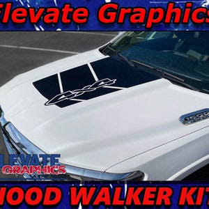 May include: White pickup truck with a black and white hood graphic that says "4x4". The truck has a "1500 HEMI 5.7L" emblem on the side.