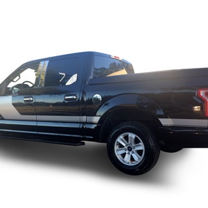 May include: Black Ford F-150 pickup truck with silver and black side stripes. The truck has a crew cab and a short bed.