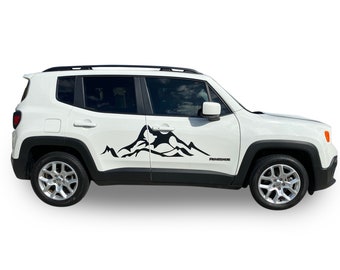 May include: White Jeep Renegade with a black mountain range decal on the side of the vehicle. The decal is a stylized mountain range with peaks and valleys.