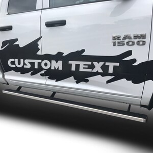 May include: A white pickup truck with a black and white graphic decal on the side that says "CUSTOM TEXT". The truck has a chrome step bar and the words "RAM 1500" on the side.