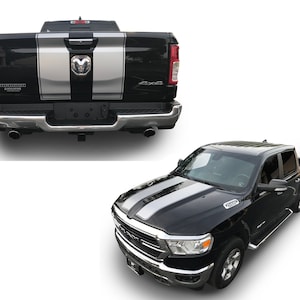Può includere: Pick-up Ram nero con strisce da corsa argentate sul cofano e sul portellone. Il camion ha un emblema 4x4 sul portellone.