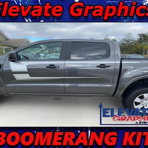 May include: A grey Ford Ranger pickup truck with a black bed and a set of grey and white boomerang decals on the sides. The truck is parked on a paved surface. The decals are labelled "Elevate Graphics" and "Boomerang Kit".