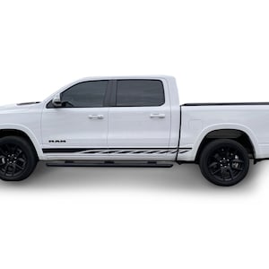 May include: White pickup truck with black wheels and tinted windows. The truck features a black and white stripe design along the side and the word "RAM" is visible. The vehicle is set against a white background.