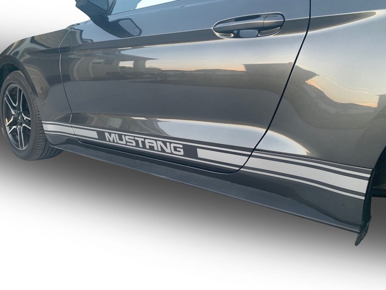 K&ouml;nnte beinhalten: Ein grauer Ford Mustang mit einem silbernen und schwarzen Seitenstreifen-Aufkleber mit der Aufschrift "MUSTANG".