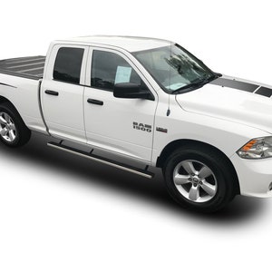 May include: White pickup truck with black racing stripes on the hood and sides. The truck has a black tonneau cover and a "RAM 1500" emblem on the side.