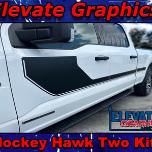 May include: A white pickup truck with black and white graphic decals on the side. The decals feature a hockey stick and the words "Hockey Hawk Two Kit". The truck has a black step bar and a "Power Stroke" emblem on the side.