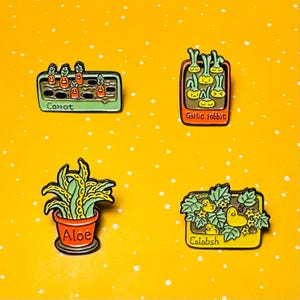 May include: Four enamel pins with a gardening theme. The pins feature a carrot patch, garlic rabbit, aloe plant, and calabash. Each pin has a black outline and is set against a yellow background with white dots.