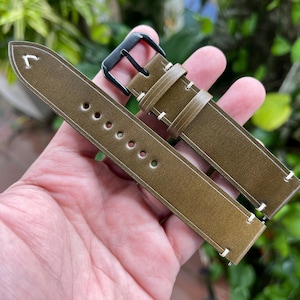 May include: A green leather watch strap with white stitching and a black metal buckle.