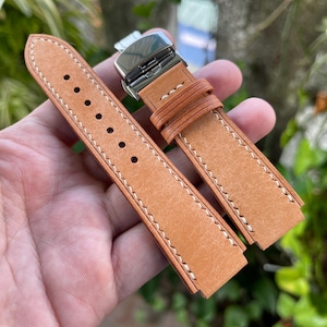 May include: Two brown leather watch straps with white stitching. One strap has a silver buckle and the other has a plain end.