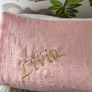 Op de afbeelding: Een roze babydeken met gouden glitter stippen en de naam "Livia" geborduurd in gouden draad.