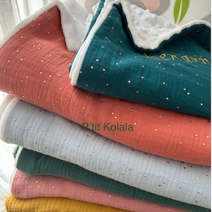 Op de afbeelding: Een stapel van zes zachte, katoenen babydekens in verschillende kleuren, waaronder koraal, teal, lichtblauw, roze en geel. Elke deken heeft een subtiel patroon van gouden stippen en een witte rand. De bovenste deken heeft de tekst "P'tit Kolala" geborduurd in goud.