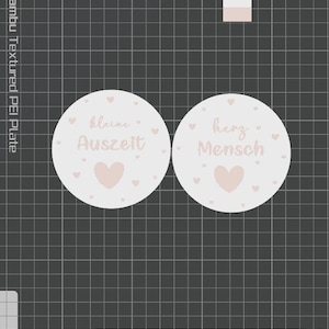 May include: Two round, light pink stickers with text and heart designs. One sticker reads "kleine Auszeit" and the other reads "herz Mensch". The stickers have a soft, pastel aesthetic, with small hearts scattered around the text and a larger heart at the bottom.