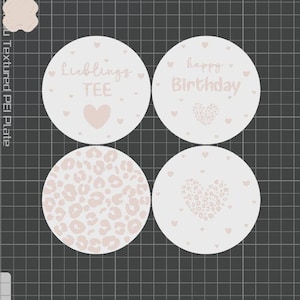 May include: Four round coasters with light pink designs on a white background. One coaster says "Lieblings TEE" with a heart, another says "happy Birthday" with a heart, a third has a leopard print, and the last has a heart design.