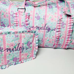 May include: A matching set of floral print travel bags in pink, blue, and purple. The larger duffel bag and smaller cosmetic bag feature vertical pink stripes, ruffles, and the name "marley" embroidered in cursive.