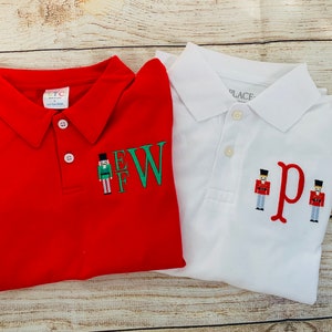 May include: Two red and white polo shirts with embroidered nutcracker designs and the letters "EW" and "p".