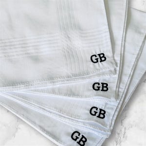 May include: A stack of white handkerchiefs with a textured pattern. Each handkerchief is embroidered with the black letters "GB" in the corner. The handkerchiefs are neatly arranged, showcasing their clean, crisp appearance.