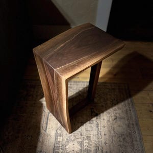 May include: A dark brown wooden side table with a curved top and a rectangular base. The table is made of live edge wood with a natural finish.