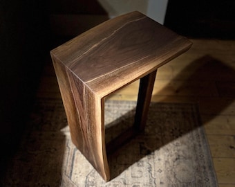 May include: A dark brown wooden side table with a curved top and a rectangular base. The table is made of live edge wood with a natural finish.