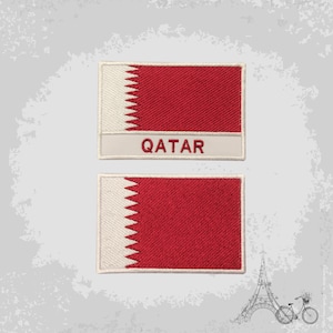 Puede incluir: Dos parches bordados de la bandera de Qatar. El parche superior tiene el texto "QATAR" debajo de la bandera. Ambos parches son blancos con un campo rojo y un triángulo blanco dentado.