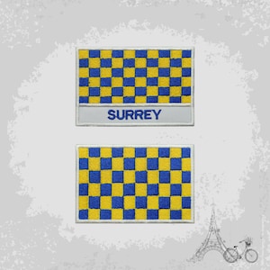 Pode incluir: Dois patches bordados com um padrão xadrez em amarelo e azul. O patch superior tem a palavra "SURREY" escrita em azul abaixo do padrão xadrez.