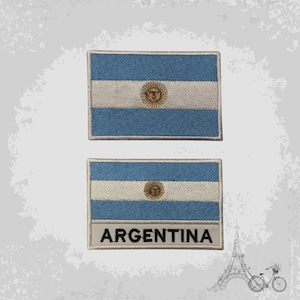 Può includere: Due toppe ricamate con la bandiera argentina. La toppa superiore è blu e bianca con un sole giallo al centro. La toppa inferiore ha lo stesso design con la parola "ARGENTINA" stampata sotto la bandiera.