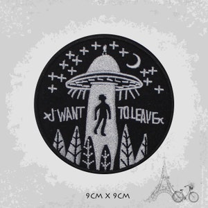 May include: A black and white embroidered patch featuring a UFO, a person, and the text "I WANT TO LEAVE". The patch measures 9 cm by 9 cm.