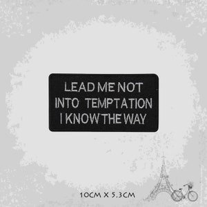 May include: Black embroidered patch with white text that reads "Lead me not into temptation I know the way". The patch measures 10 cm by 5.3 cm.