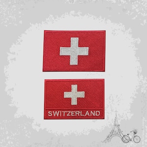 Puede incluir: Dos parches bordados rojos con la bandera suiza, una cruz blanca sobre fondo rojo. El parche inferior tiene la palabra "SWITZERLAND" bordada en blanco. Los parches son rectangulares.