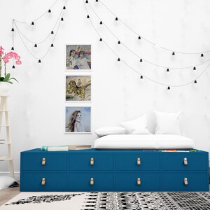 May include: A blue dresser with six drawers and gold handles. The dresser is in a bedroom with a white wall, a white bed, and a globe light hanging from the ceiling.