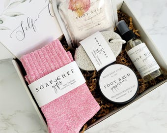 May include: A gift box containing a pair of pink ribbed socks, a bag of Himalayan pink salt foot soak, a pumice stone, a bottle of peppermint foot mist, and a container of peppermint foot balm, all labeled with Soap Chef Gifts branding.