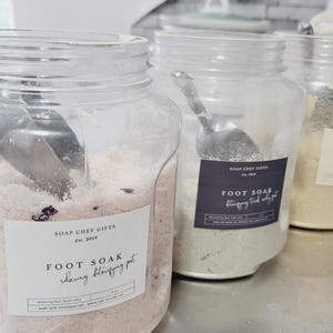 May include: Three clear plastic jars filled with different colored bath salts. The jars have labels that say "Soap Chef Gifts Est. 2019" and "Foot Soak Relaxing, Detoxifying  Pot".