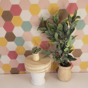 May include: Two potted plants on a wooden table with a white base. The larger plant has green leaves and is in a wooden pot. The smaller plant is a succulent in a brown pot. The background is a white wall with a geometric pattern of pink, yellow, brown, and blue hexagons.